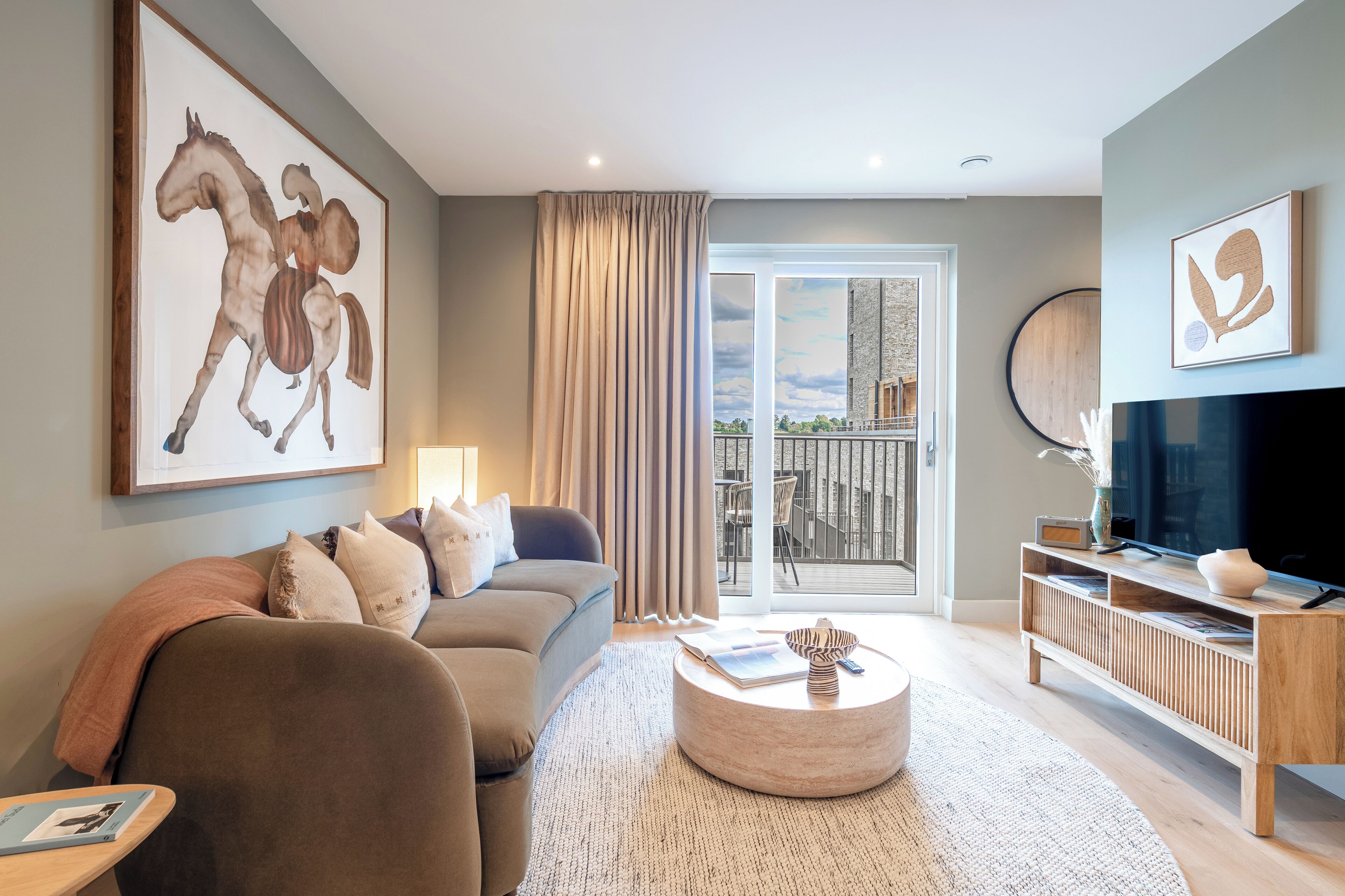 A modern living room with a sofa, a coffee table, a TV, and a large window with curtains.