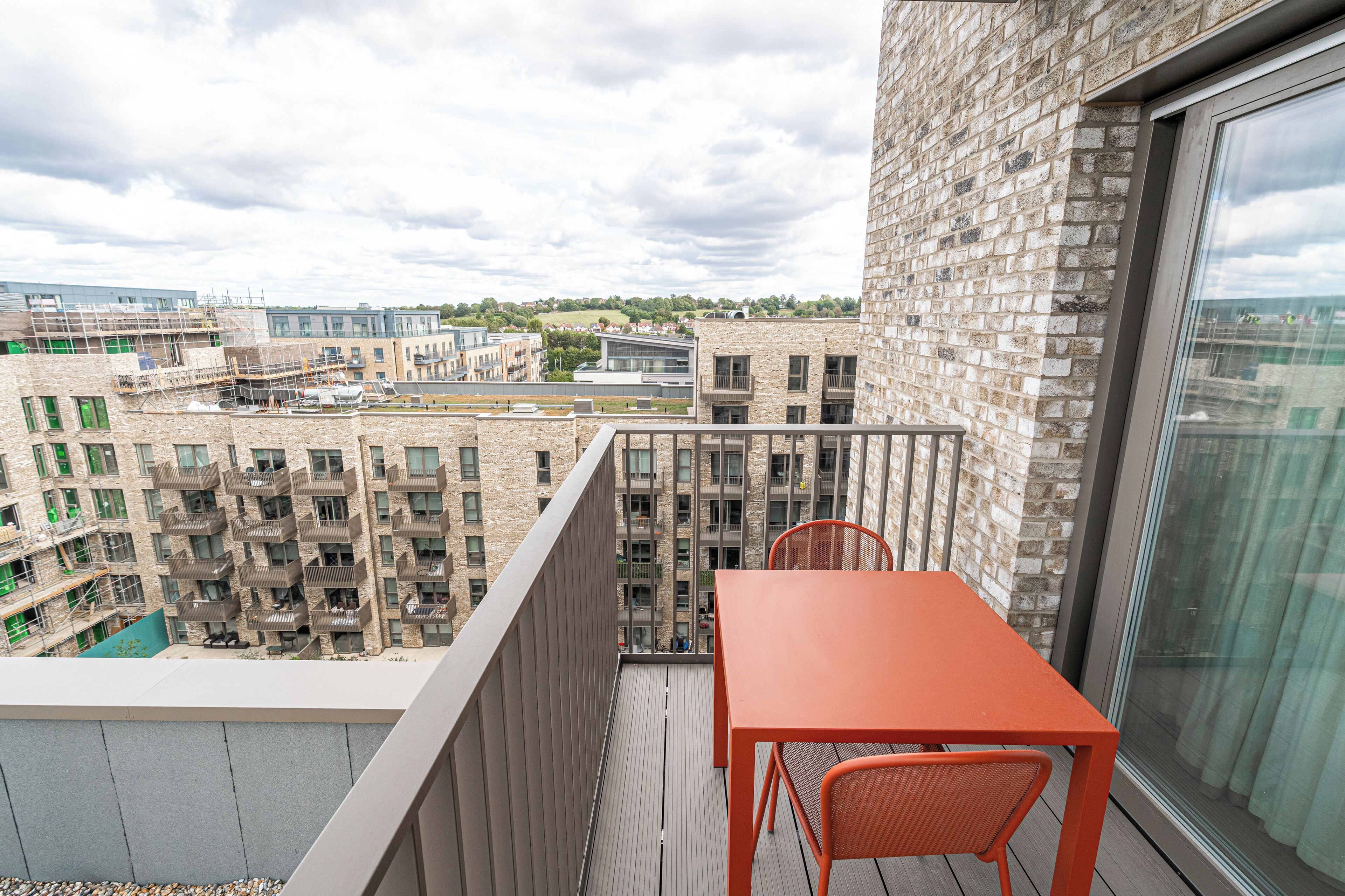 A balcony with a table and chairs, overlooking a cityscape with modern buildings and a green park.