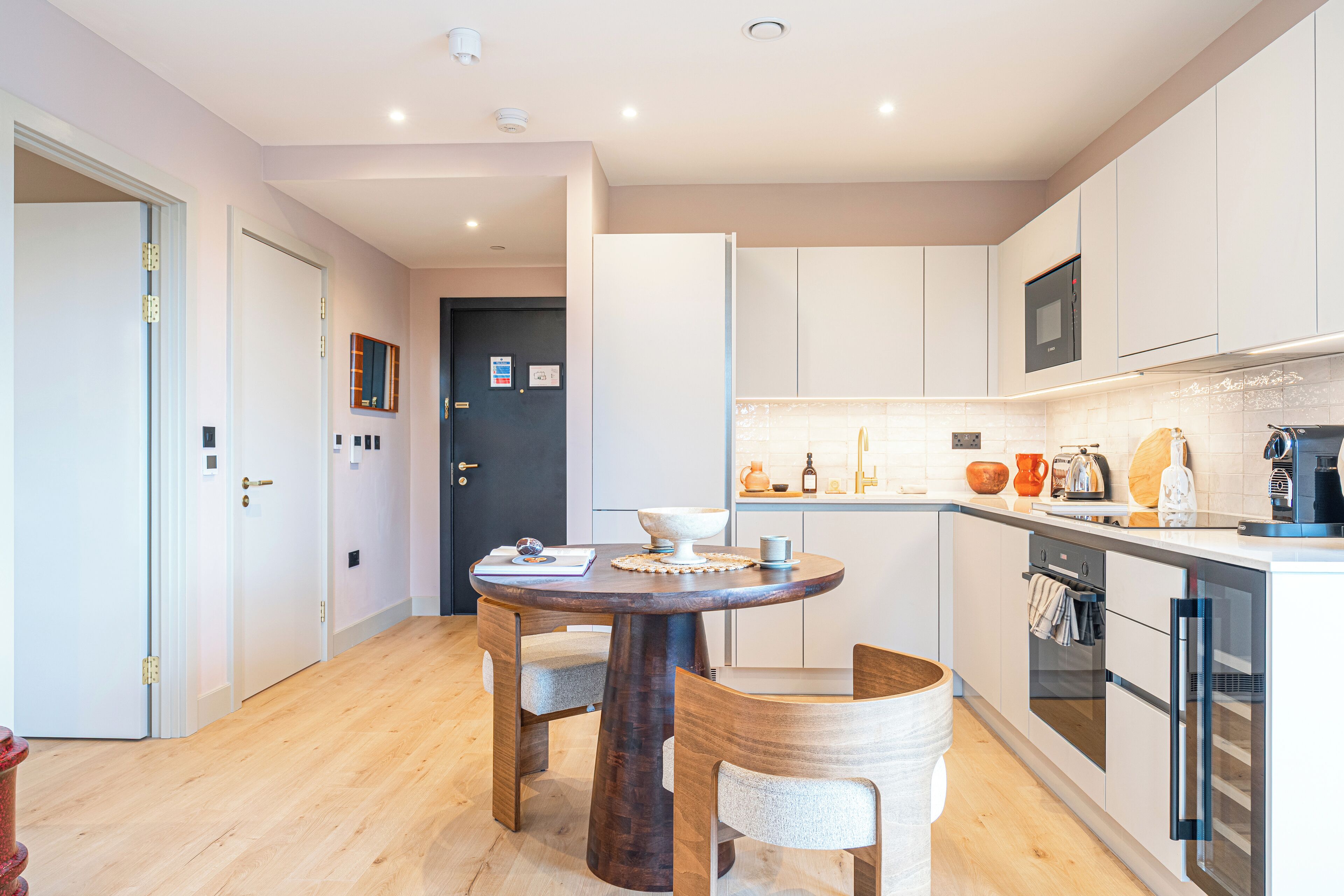 A modern kitchen with a round wooden table, white cabinets, and a built-in oven.