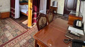 A hotel room with a four-poster bed, a dining table, a television, and a telephone. - Ak zhol (Almaty)