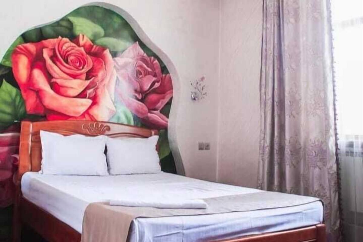 A bedroom with a bed, a large floral mural on the wall, and a window with curtains.