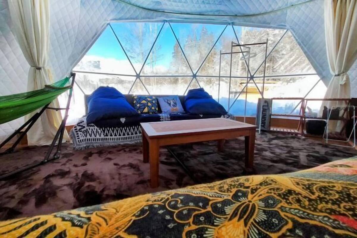 A cozy interior with a hammock, a cushioned seating area with pillows, a wooden table, and a patterned rug.