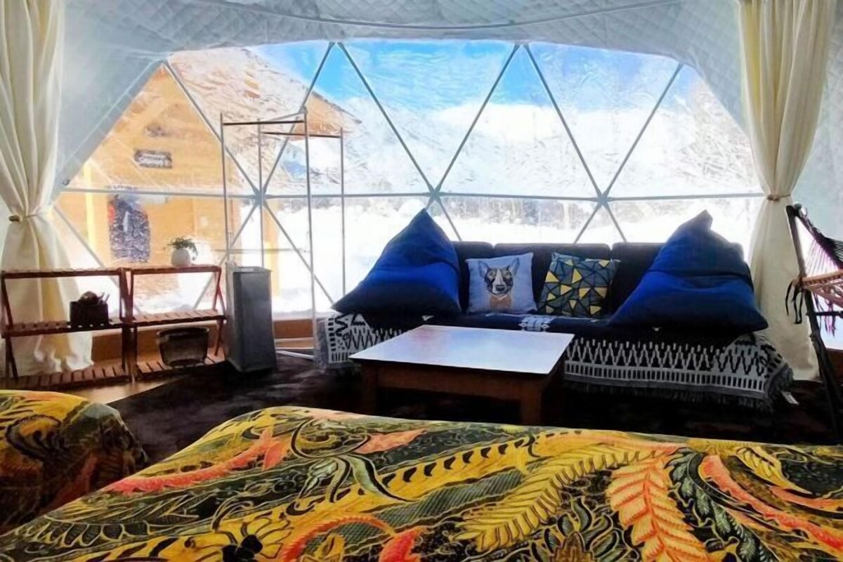 A cozy room with a large window, a sofa with blue cushions, a patterned rug, and a small table.