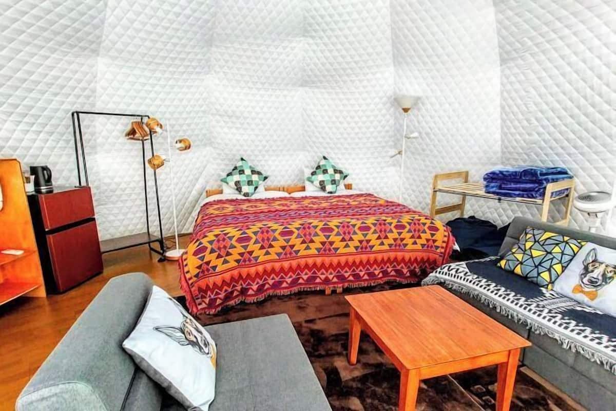 A cozy room with a bed, a sofa, a table, and a small wooden cabinet.