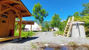 A wooden cabin with a covered outdoor seating area, a sauna, and a large water tank. - Glamping+Sauna Hakuba morino wasabi nouen (Kitaazumi District)