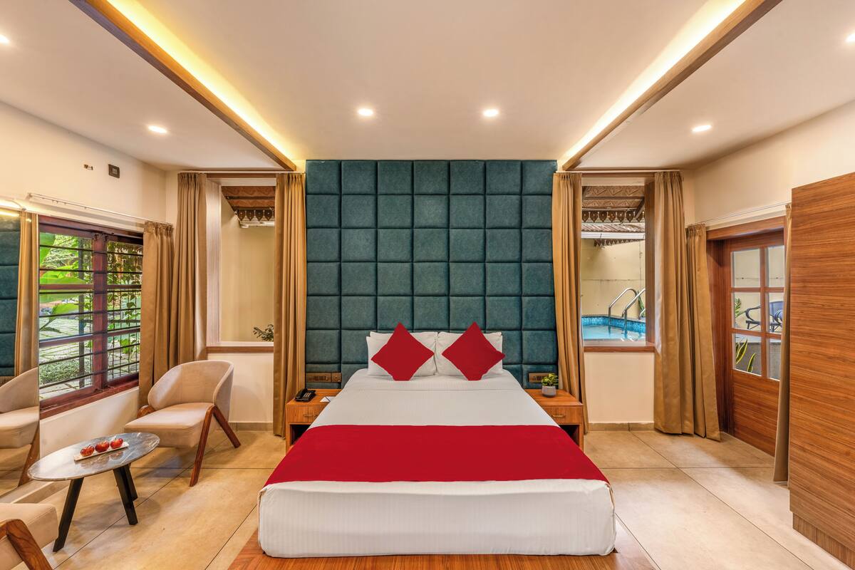 A spacious bedroom with a large bed, two bedside tables, a nightstand, a small round table, and a view of a swimming pool.