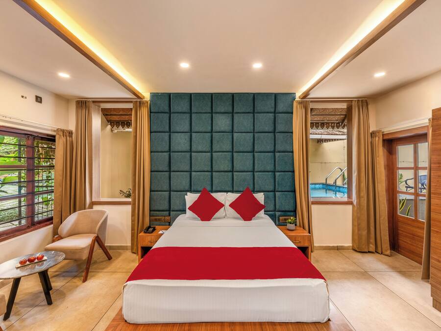 A spacious bedroom with a large bed, two bedside tables, a nightstand, a small round table, and a view of a swimming pool.