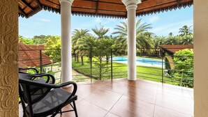 Ein überdachter Balkon mit Blick auf einen Pool, weiße Säulen und schwarze Korbstühle.