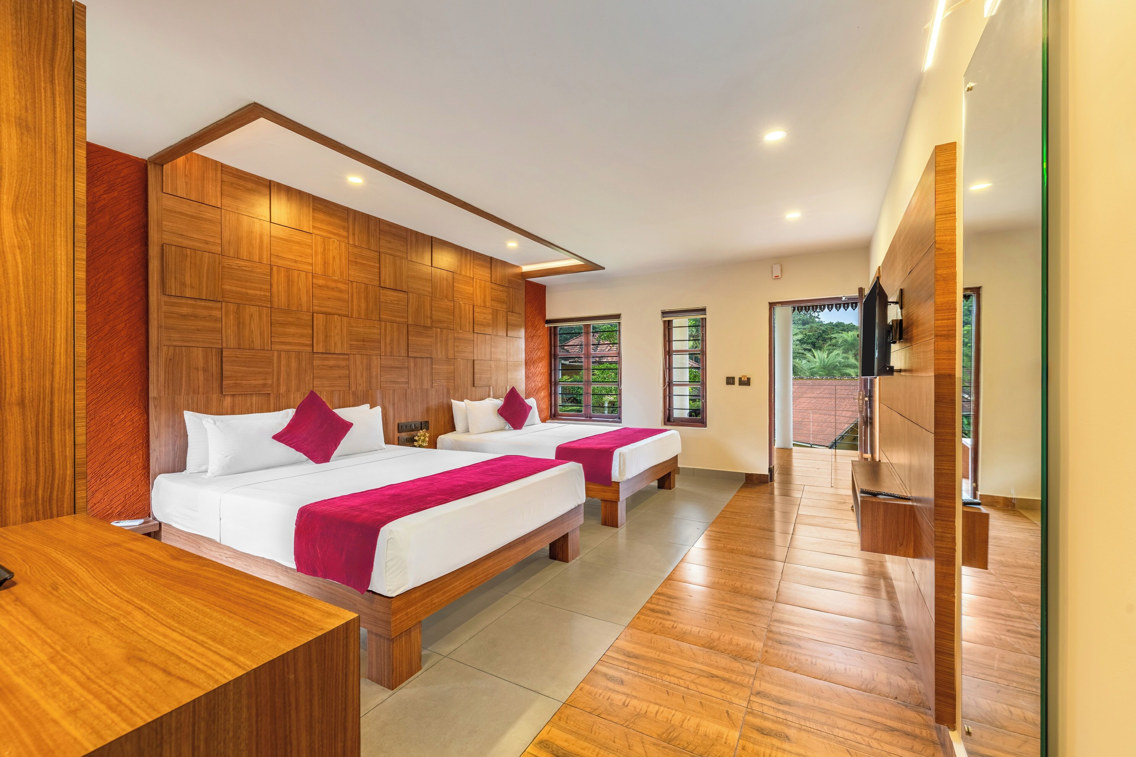 A modern hotel room with two beds, wooden paneling on the walls, and a large window providing a view of greenery.