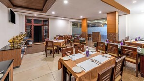 Ein Restaurant mit Holztischen, -stühlen und einer Buffetinsel mit goldenen Serviergeschirr.