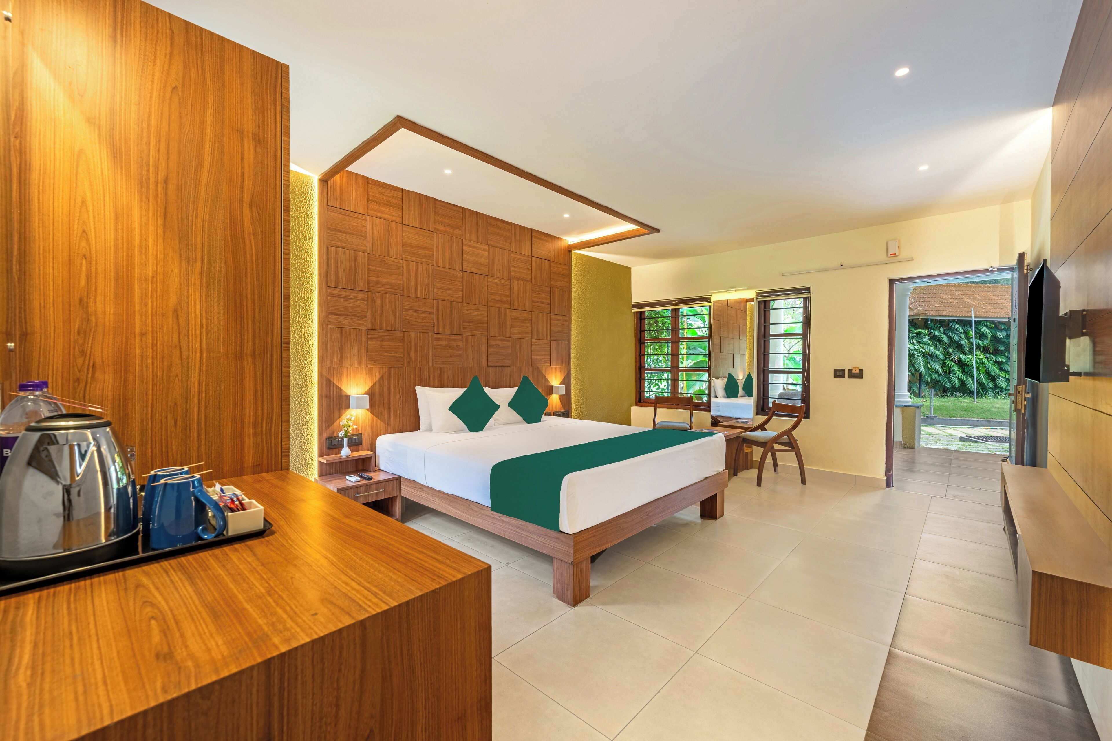 A modern hotel room with a wooden bed, a desk with a kettle, and a TV.