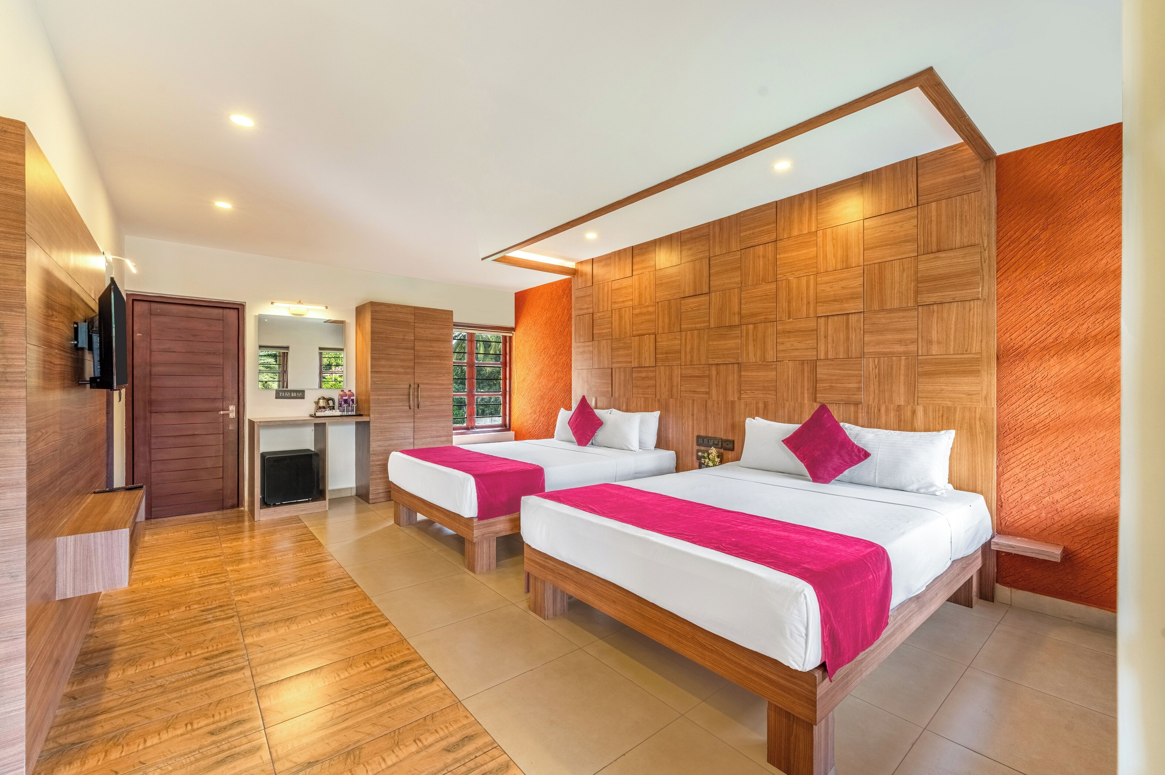 A modern hotel room with two beds, wooden headboards, a flat-screen TV, and a small desk area.