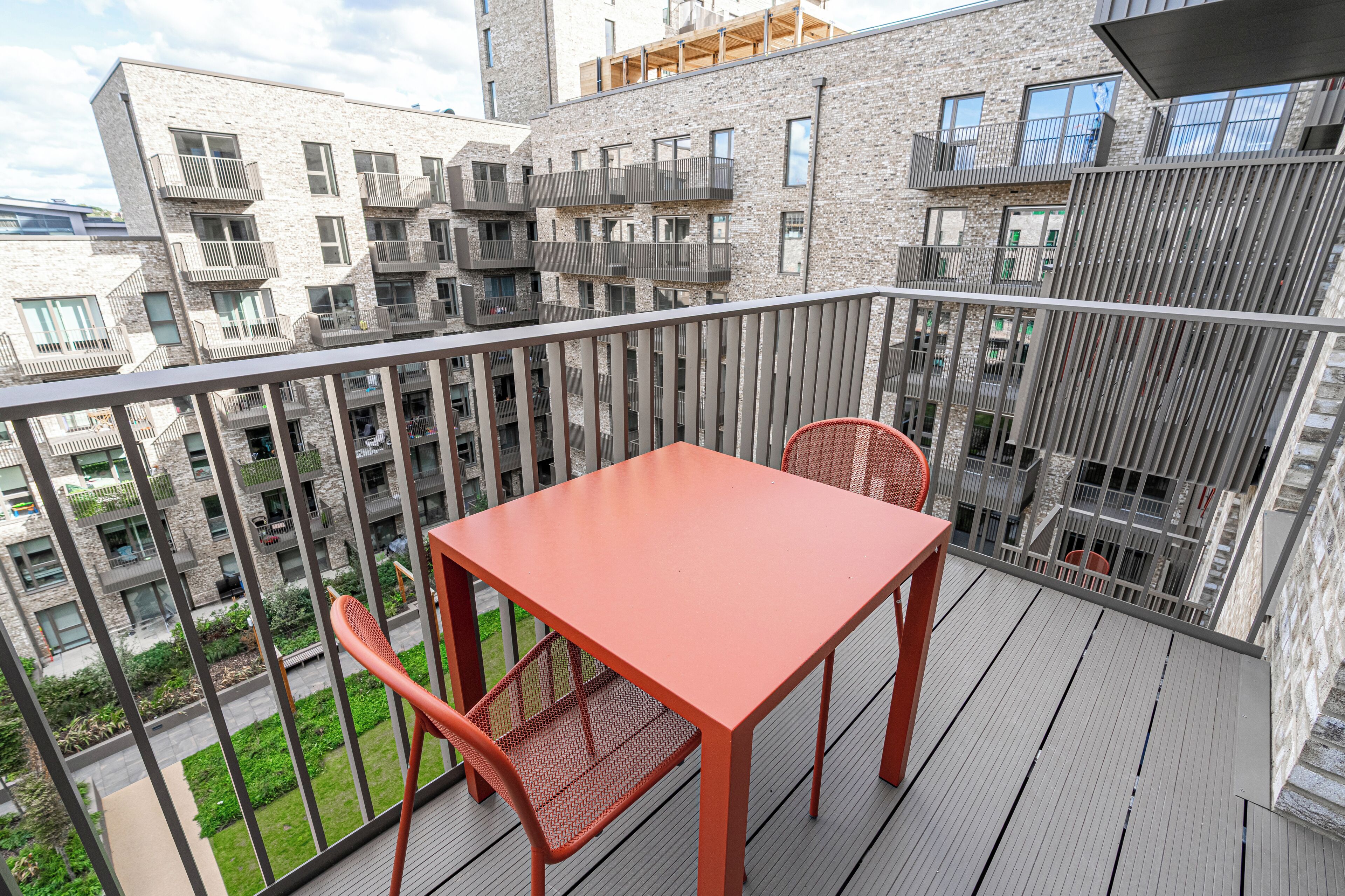 A balcony with a table and chairs, overlooking a residential area with modern buildings.