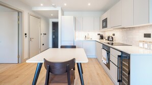 A modern kitchen with white cabinets, a stainless steel sink, and a dining area with a white table and two chairs. - Stylish One-bedroom Haven (London)