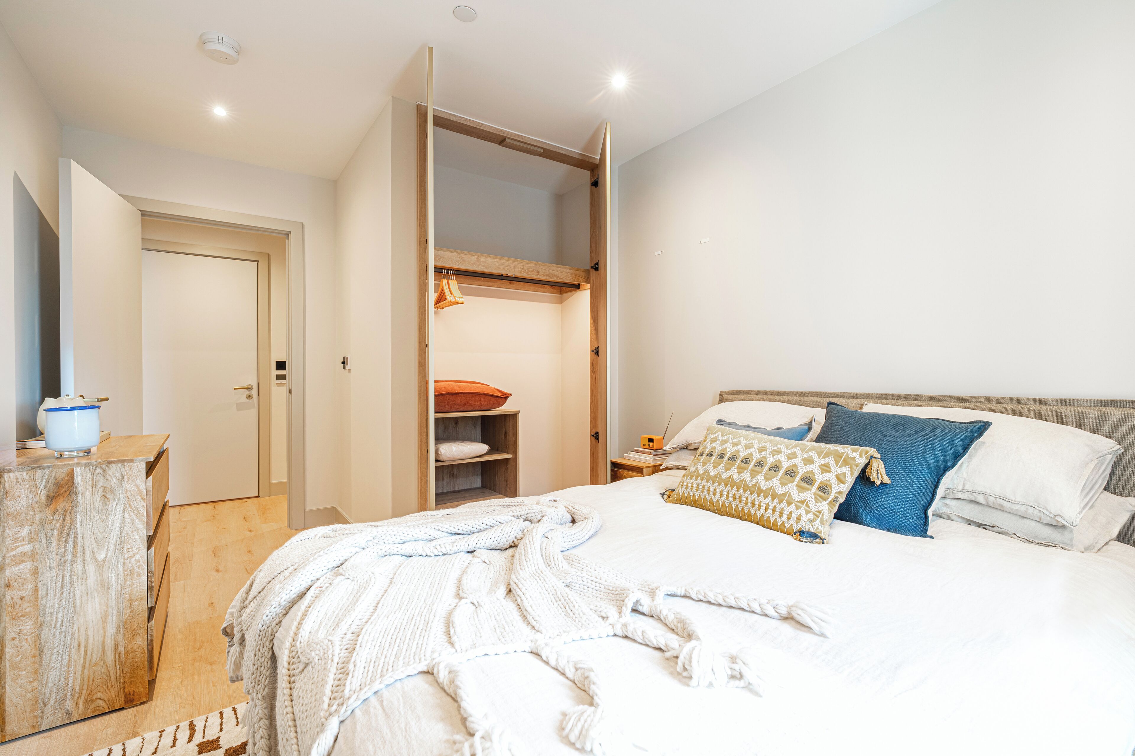 Ein Schlafzimmer mit Bett, Nachttisch und einem offenen Kleiderschrank mit Regalen.