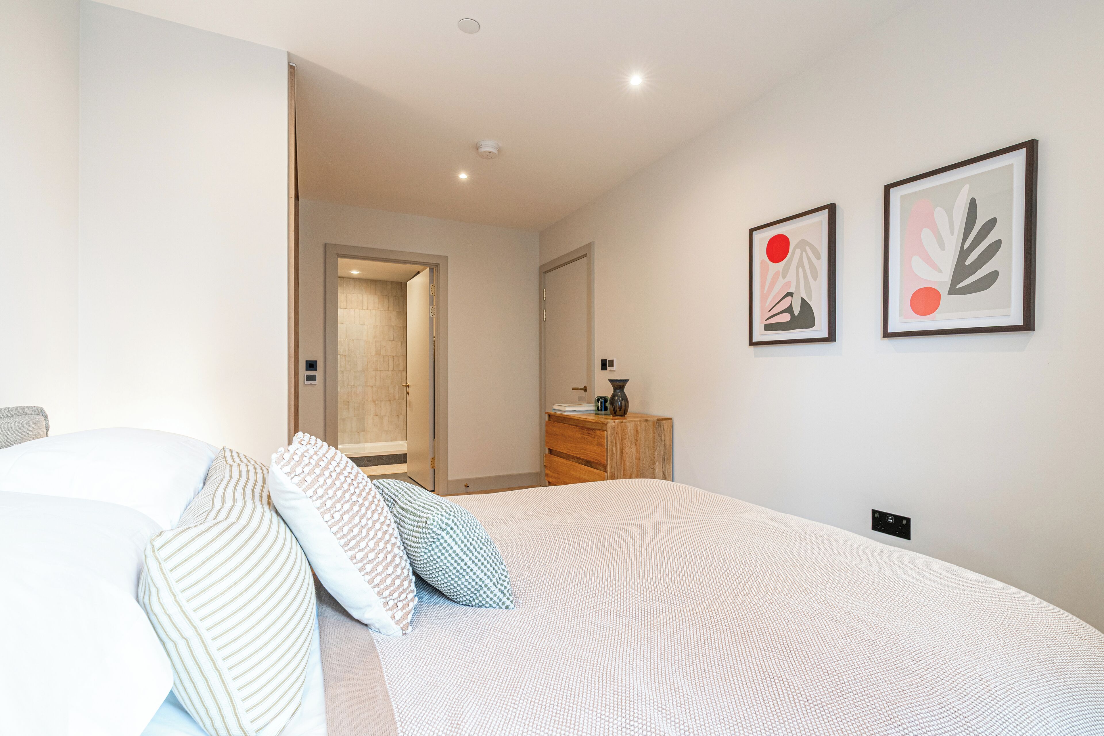 A bedroom with a bed, pillows, a dresser, and two framed artworks on the wall.