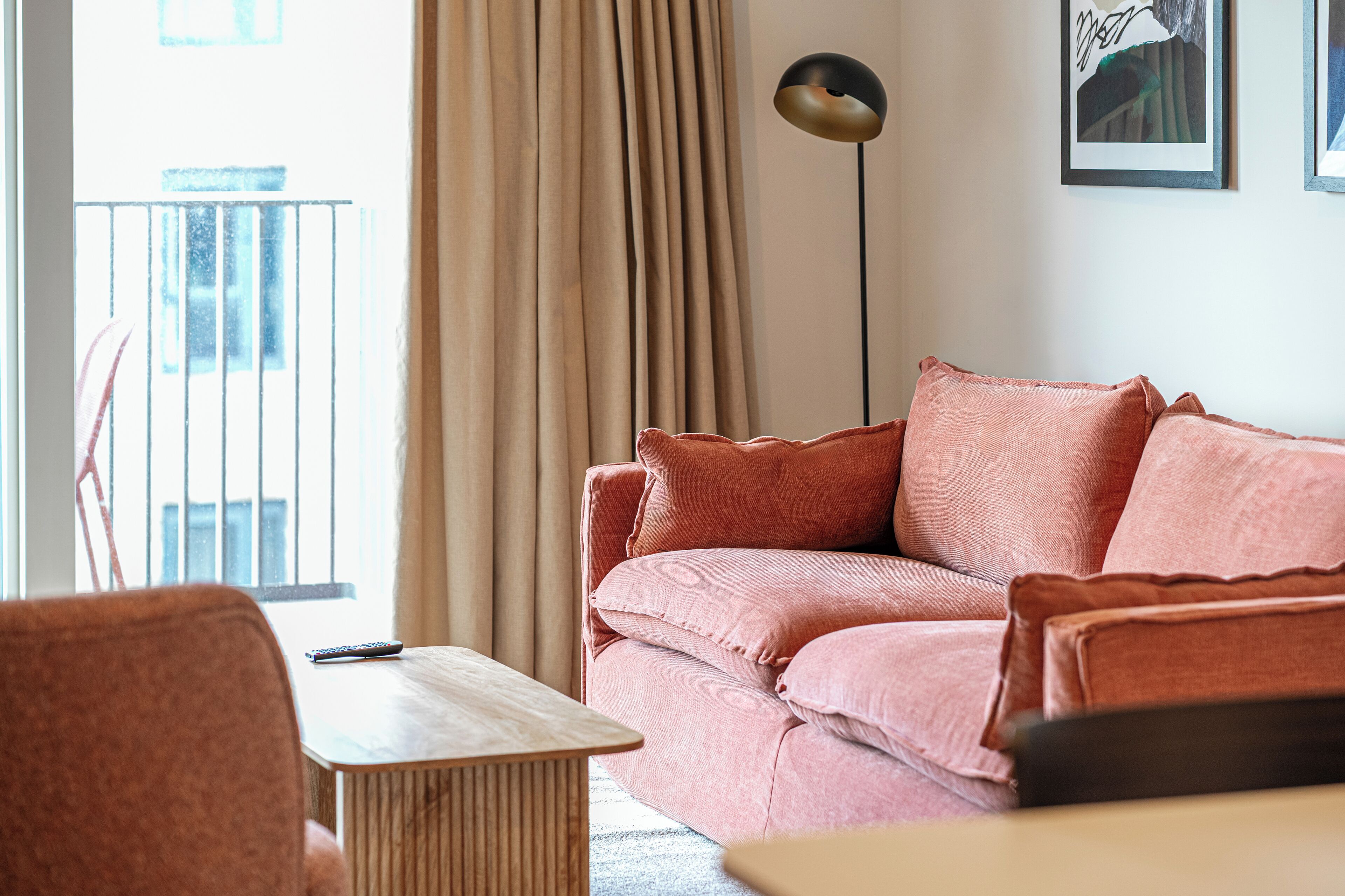 A living room with a pink sofa, a wooden coffee table, a floor lamp, and a framed picture on the wall.
