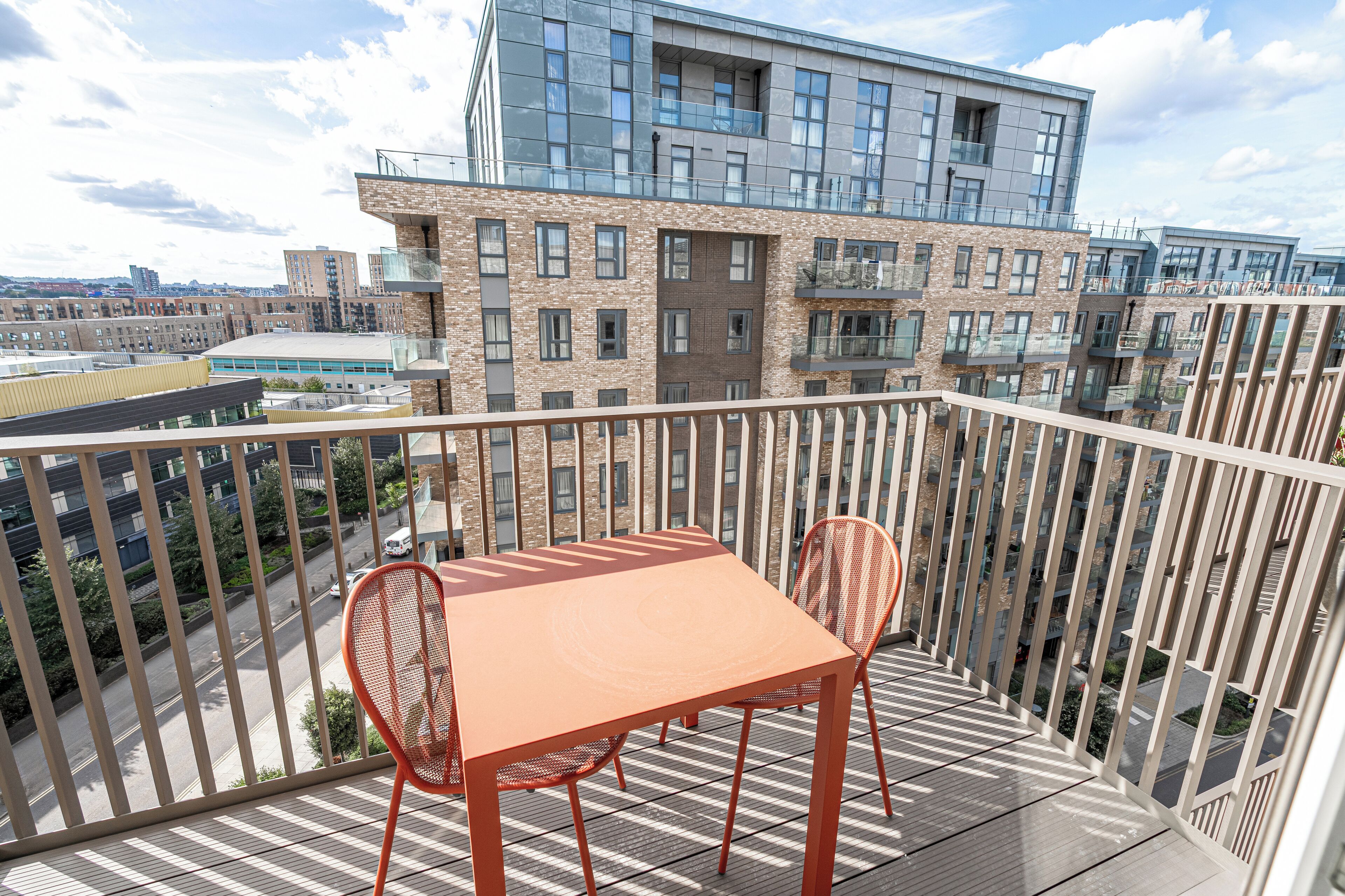A balcony with a table and chairs, overlooking a modern building and a street.