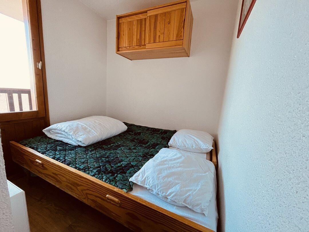 A small, single-bed room with a wooden headboard, a window, and a wooden cabinet above the bed.