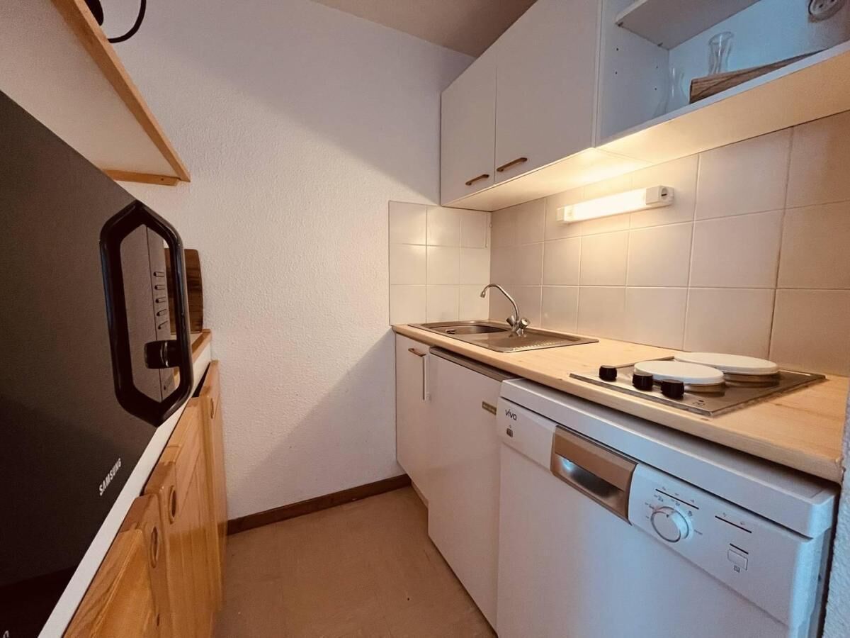 A compact kitchen with a dishwasher, stove, and a microwave on a wooden cabinet.