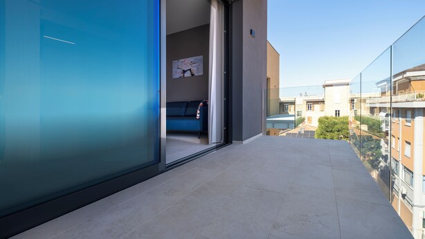 A modern balcony with a glass door leading to a room with a blue sofa and a painting on the wall. - G PALACE Residence (Civitanova Marche)