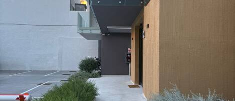 A modern building with a glass balcony, a concrete pathway, and some greenery.