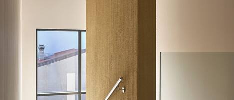 Un interior moderno con una pared texturizada, una puerta de vidrio que da al exterior y una barandilla de metal.
