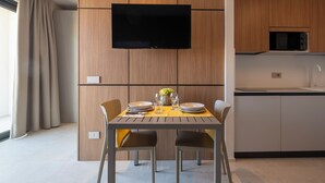 A modern kitchen with a flat-screen TV mounted above the counter, wooden cabinetry, and a dining area with a table set for two. - G PALACE Residence (Civitanova Marche)