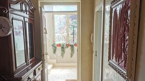 A hallway with a wooden cabinet, a clock, and a door leading to a room with a window and plants. - Cilento sea and history - Double (San Marco)