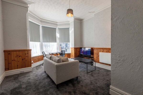 A living room with a grey sofa, wooden paneling, a television, and a large window. - St Andrews by Guestz (Lytham St. Anne's)