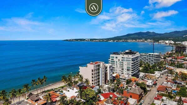 A coastal cityscape with modern buildings, a beach, and palm trees. - New Stylish 1 BR Condo - Ocean Views - Flex Room (Bucerías)