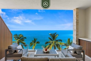 A balcony with a view of the ocean, palm trees, and a table with a candle.