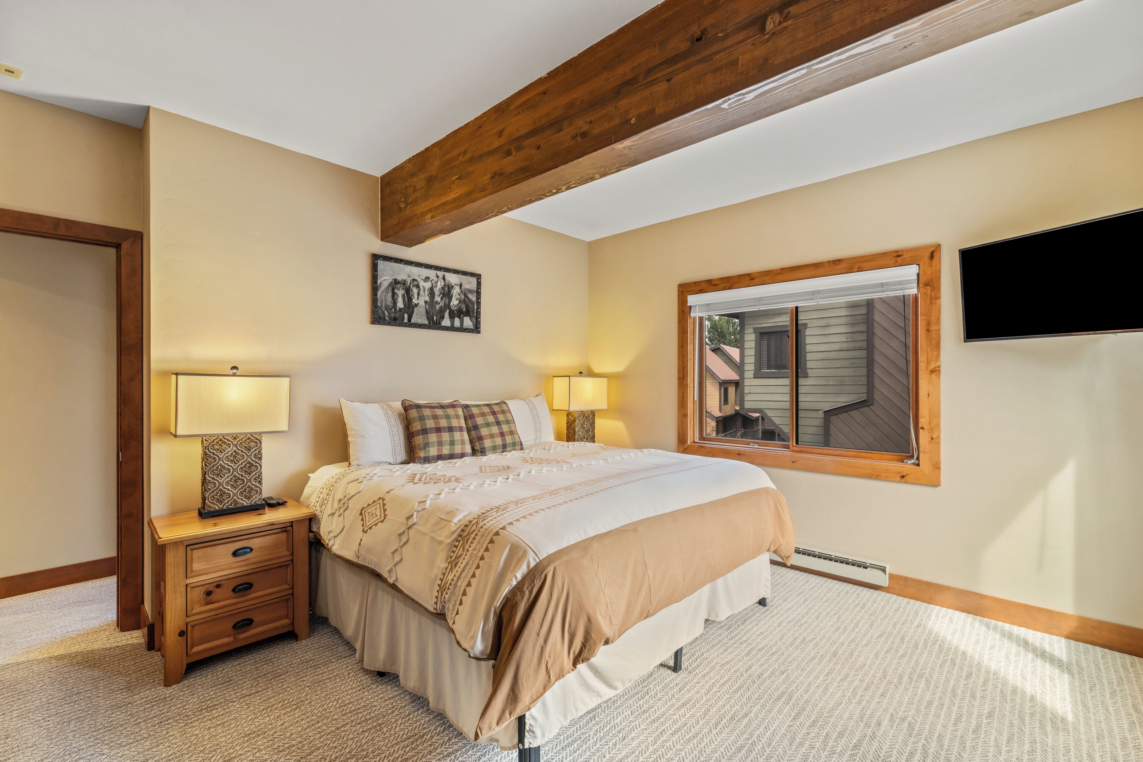 Un dormitorio con cama, lámparas de noche, mesita de noche, ventana y televisor montado en la pared.