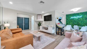 A modern living room with a sofa, coffee table, and a TV mounted on the wall. There is a gaming console and a neon sign on the wall. - Paradise Found Home With Private Heated Saltwater Pool And Cabana Plus Game Room (Seminole)