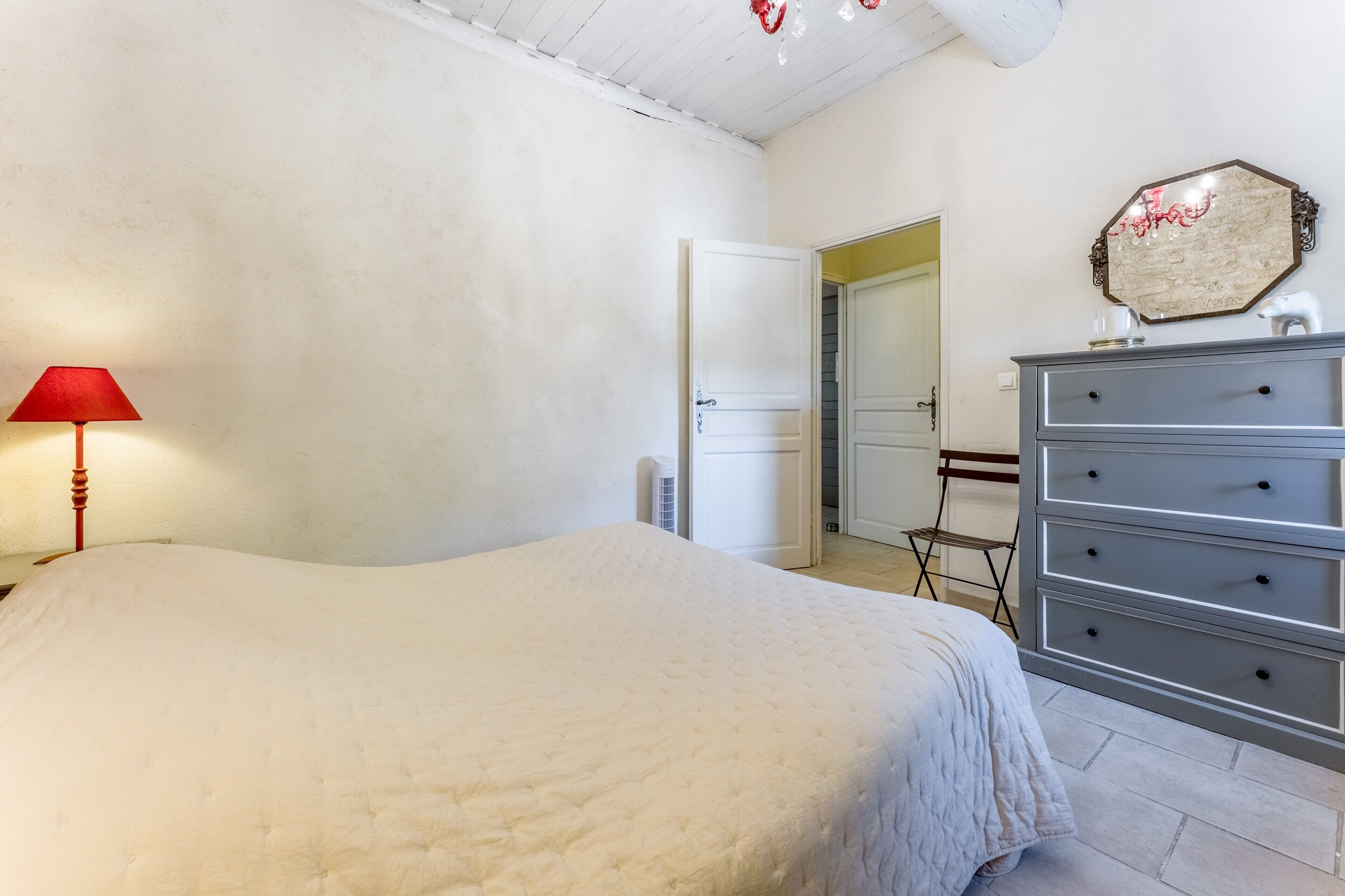 Une chambre à coucher comprenant un lit, une commode, une lampe et une porte donnant sur une autre pièce.