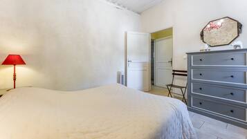 Une chambre à coucher comprenant un lit, une commode, une lampe et une porte donnant sur une autre pièce.