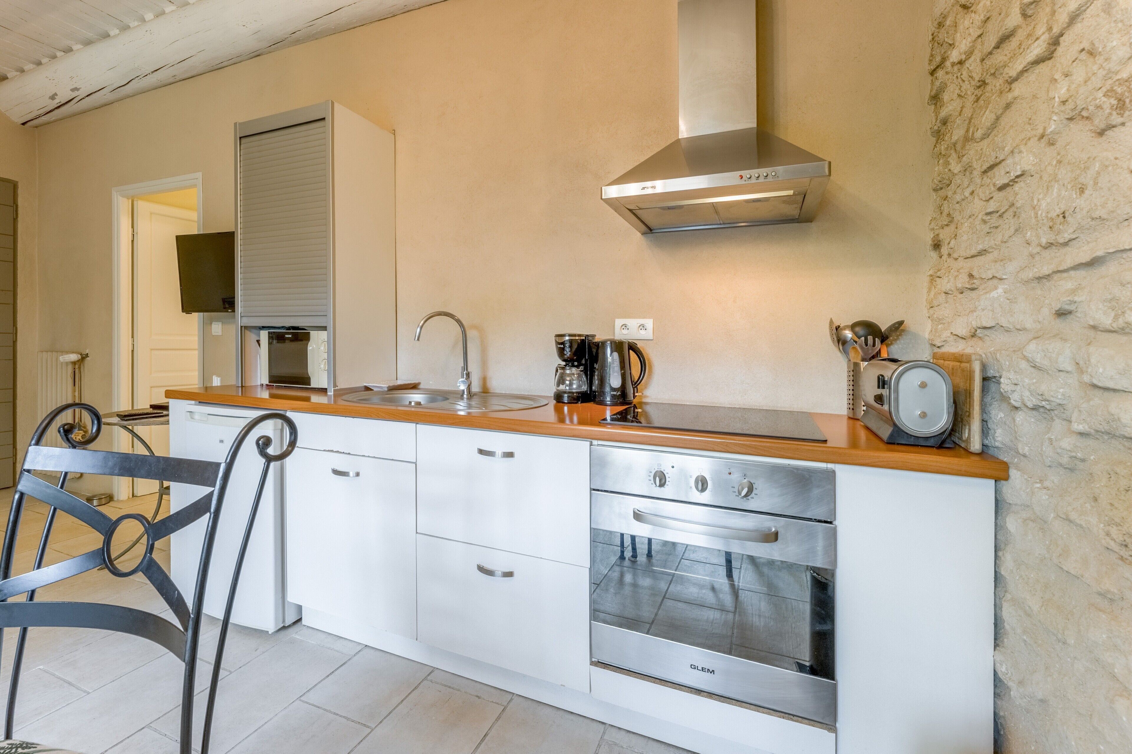 A modern kitchen with white cabinets, stainless steel appliances, a wooden countertop, and a stone wall.