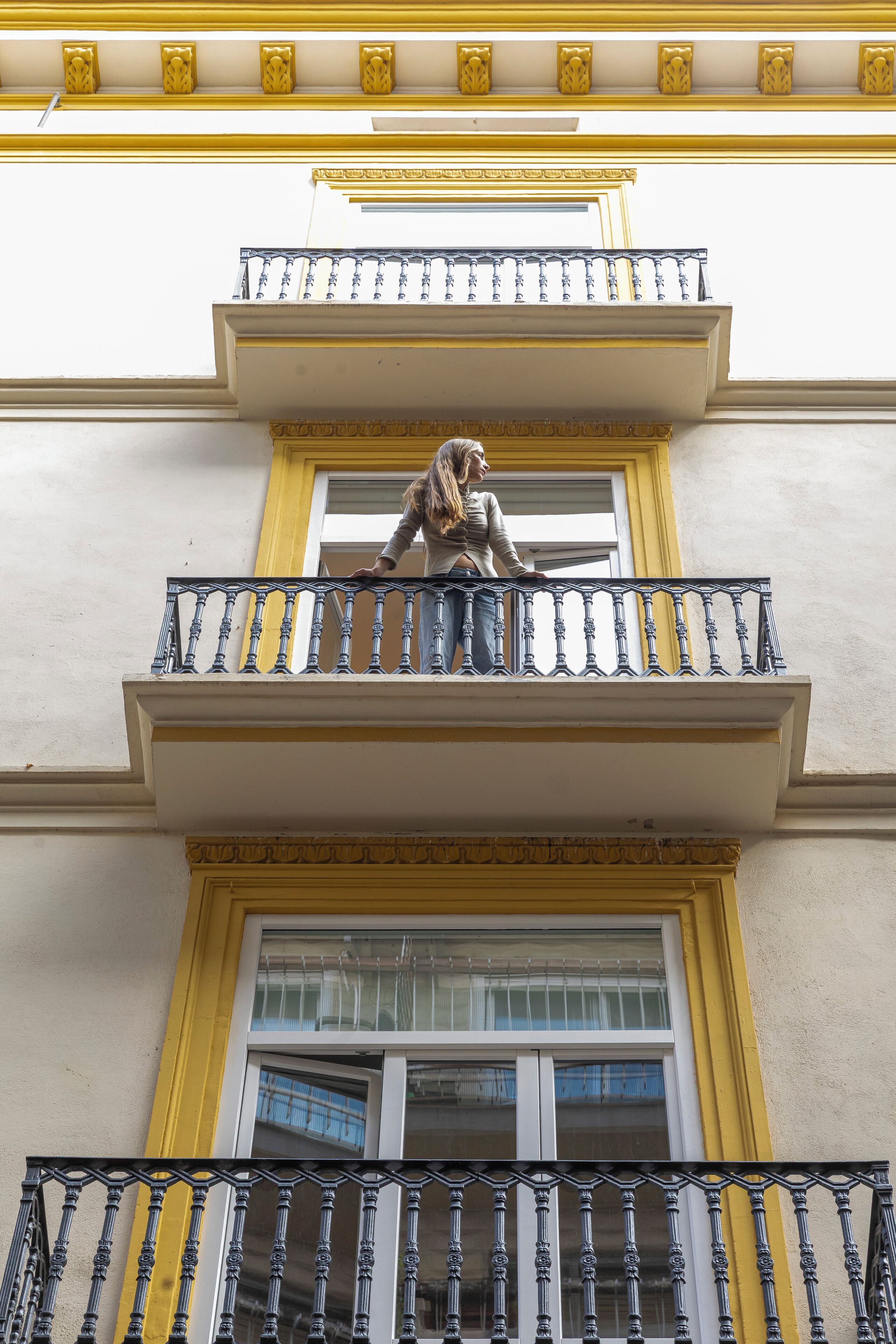 Fachada de edificio con un balcón que presenta barandillas ornamentales y detalles en amarillo.