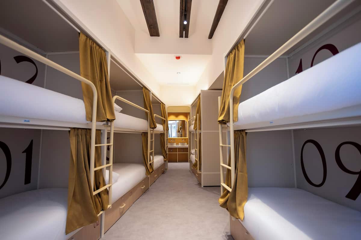 A narrow corridor with bunk beds numbered 01 to 09, a central sink, and a small window.