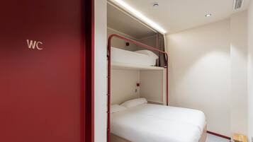 Dormitorio con literas, un armario rojo etiquetado como 'WC' y un taburete de madera pequeño.