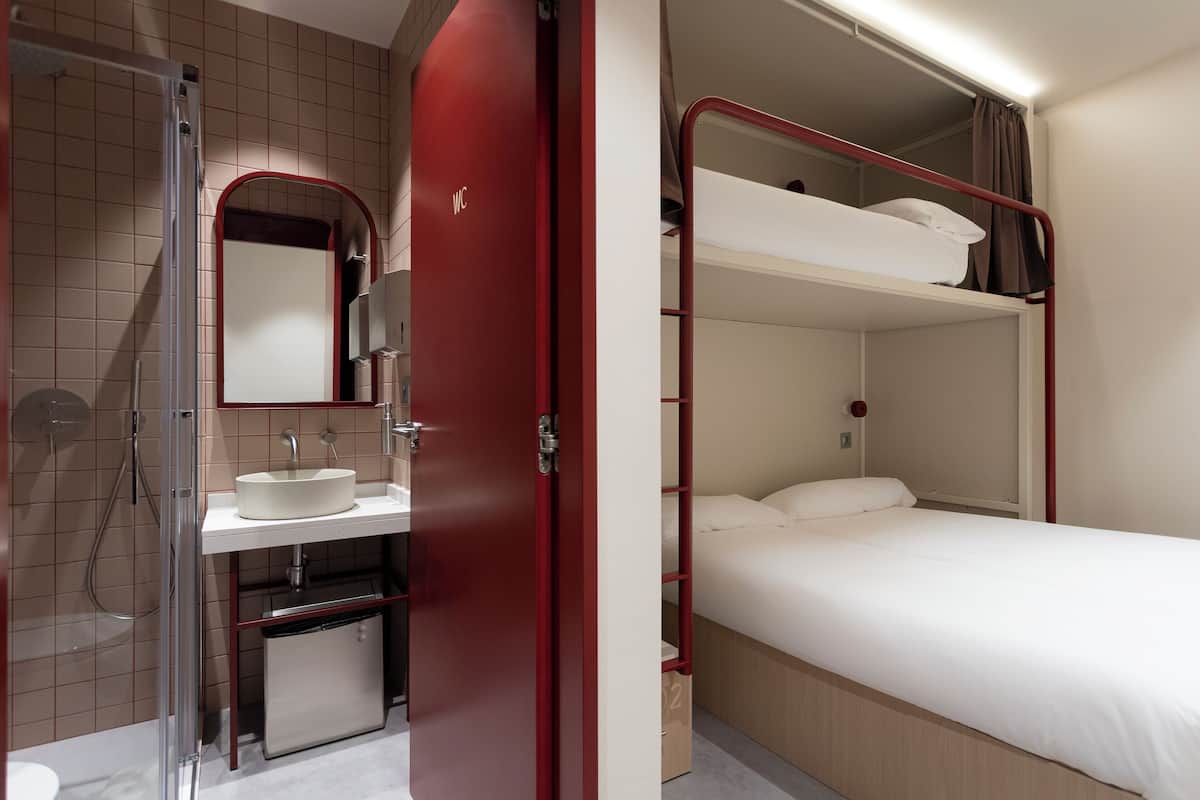 A compact hotel room with a shower, sink, and a bunk bed.