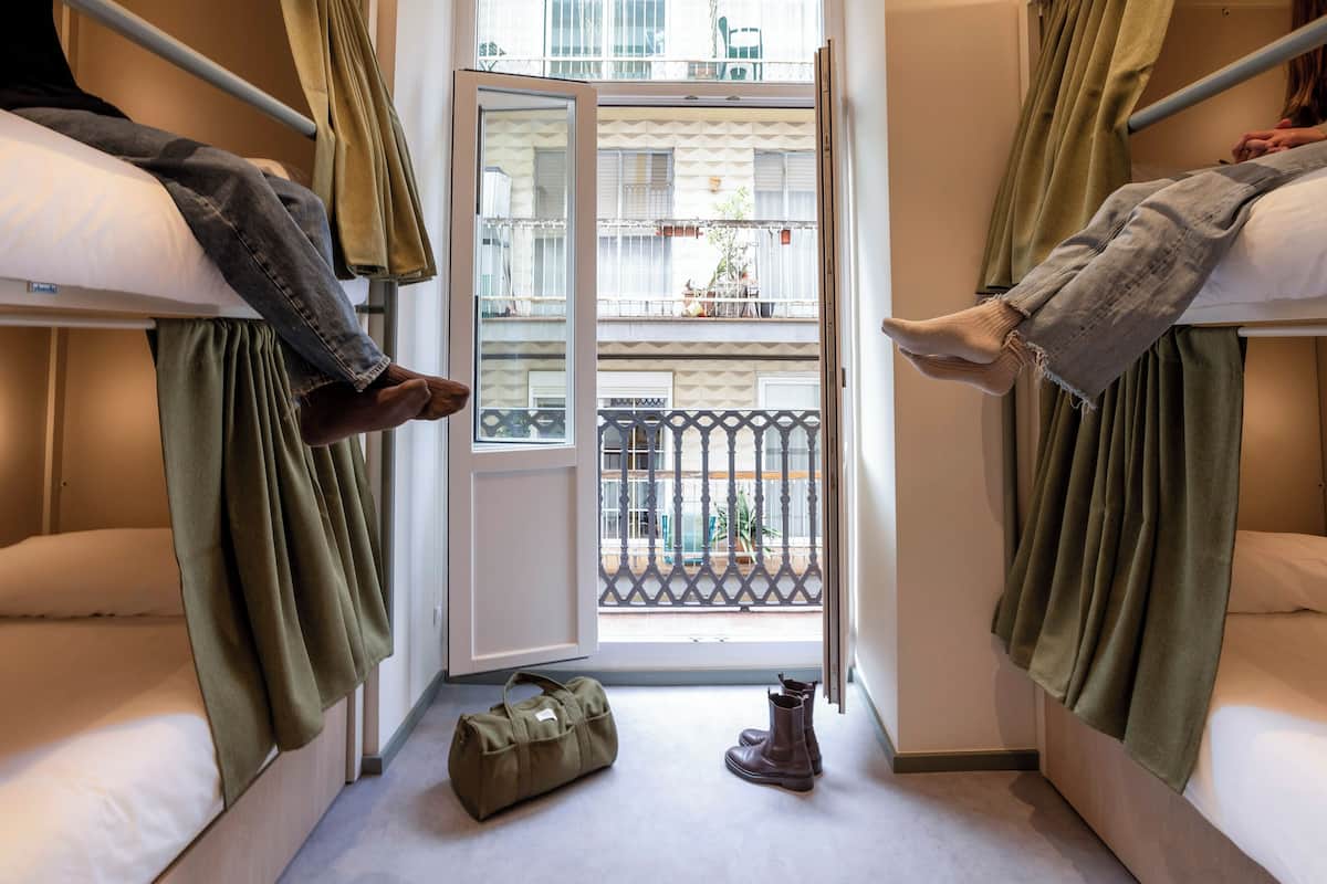 A room with bunk beds, a balcony, a door, and a pair of boots and a bag on the floor.