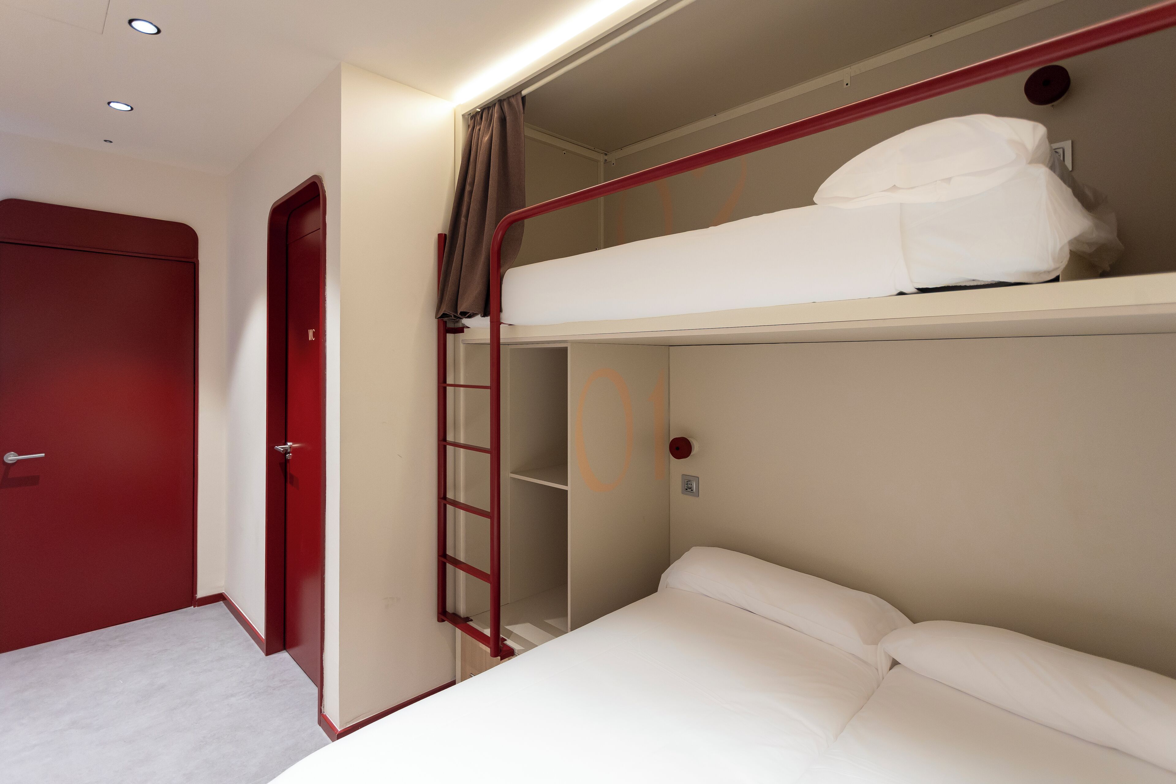 Una cama litera con escalera, una puerta roja y una pared blanca.