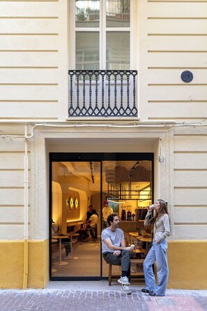 Un café doté d’une terrasse, d’une entrée avec une porte vitrée et d’un petit balcon situé au-dessus de la porte.