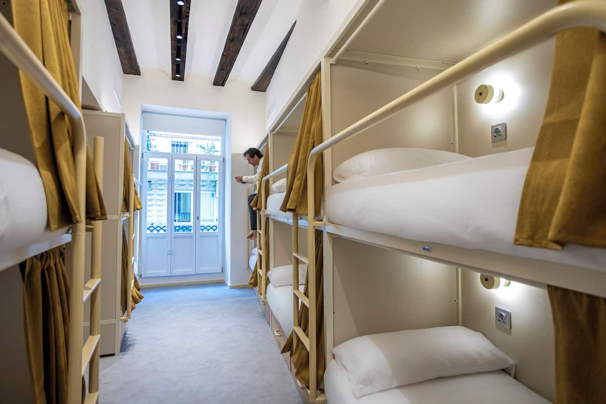 A narrow corridor with bunk beds, a door leading outside, and a person standing by the door.