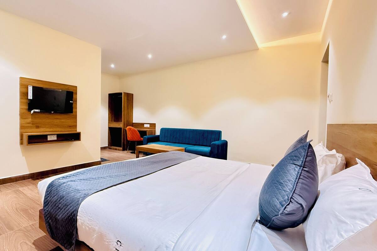 Una habitación de hotel con una cama, un televisor montado en la pared, un sofá azul y un escritorio de madera.