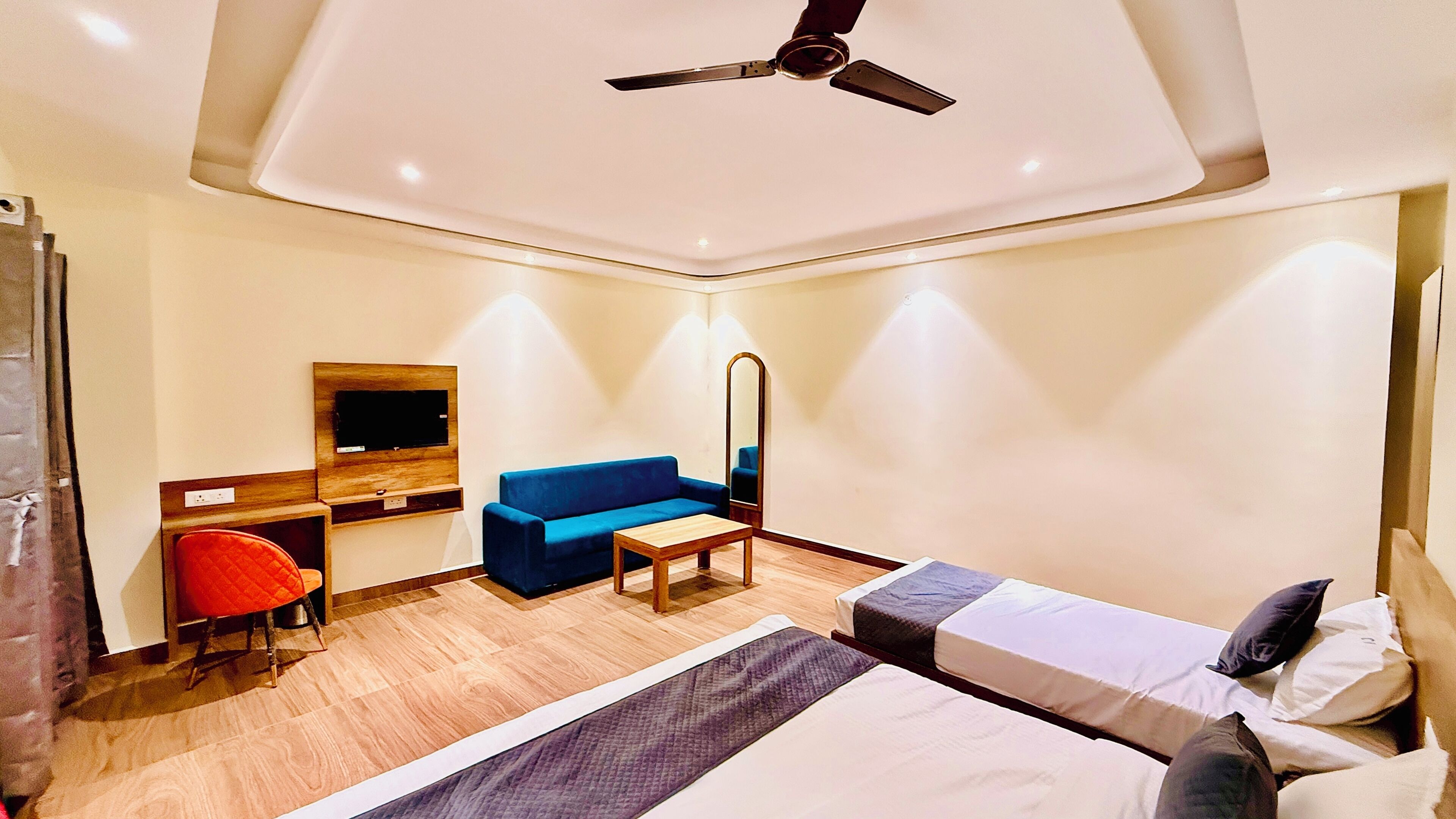 Una camera d'albergo con un letto, una scrivania con una sedia, un divano, una ventola a soffitto e uno specchio.
