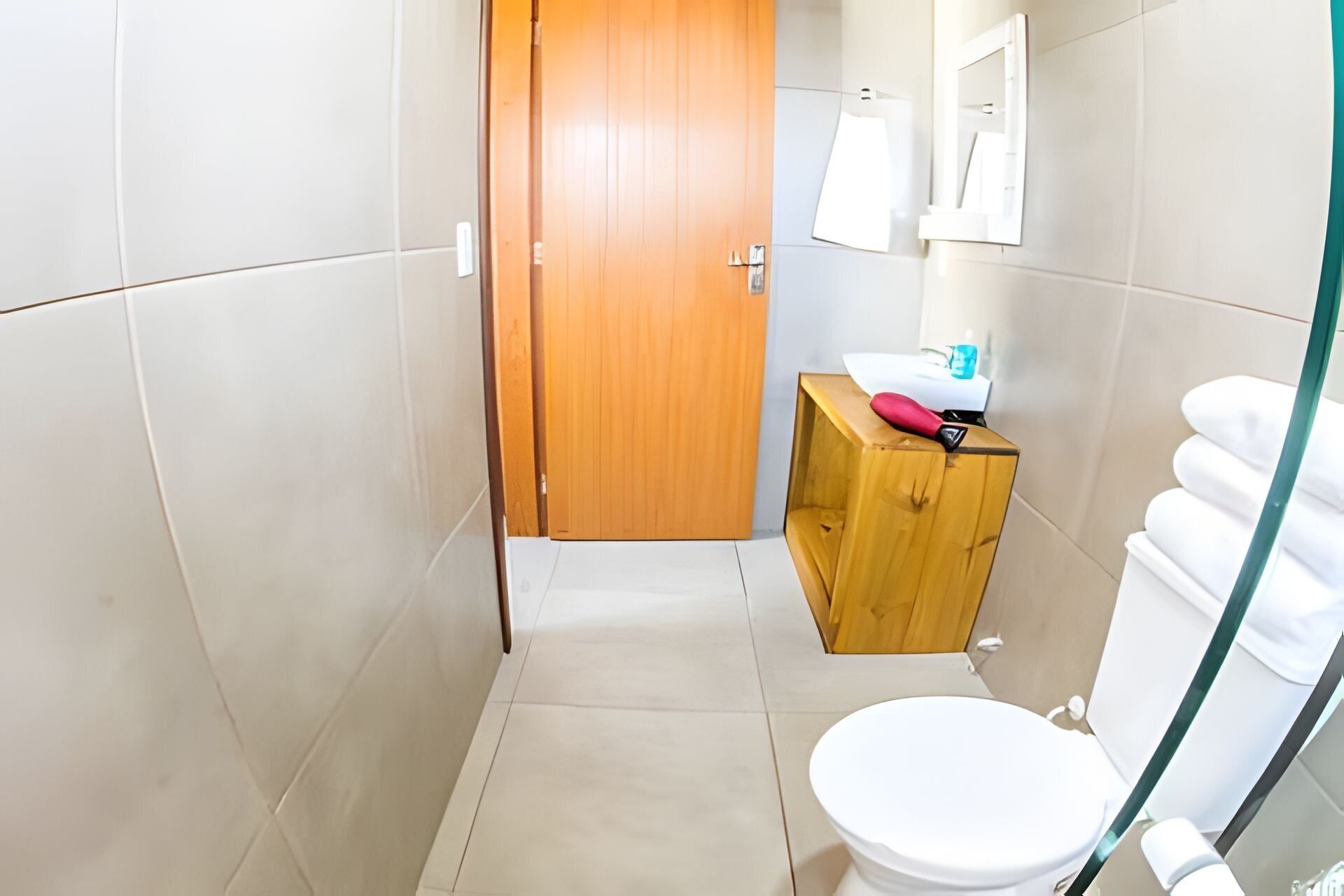 Un baño pequeño y estrecho con una puerta de madera, un inodoro blanco y un mueble de madera con un espejo arriba.