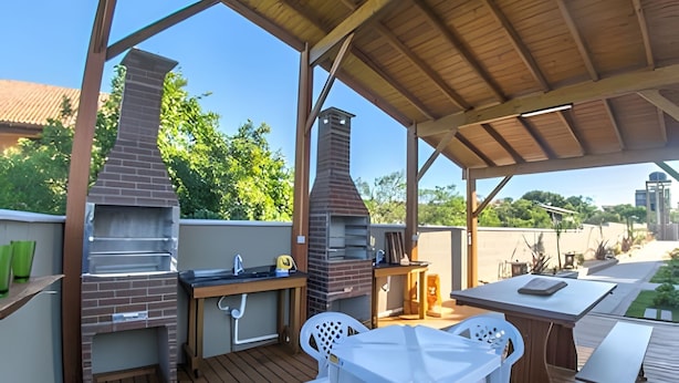 Une terrasse extérieure dotée d’un four à briques et d’un barbecue, d’une terrasse en bois et de chaises en plastique blanches.