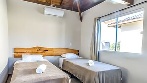 Une chambre avec deux lits simples, une tête de lit en bois, une fenêtre avec des rideaux et un ventilateur de plafond.